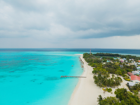 Aerial view of turquoise waters meet the pristine white sands of the beach fringed by lush greenery under a cloudy sky Vashafaru Island Thiladhummathi Atoll Maldives. Aerial view of turquoise waters meet the pristine white sands of the beach fringed by lush greenery under a cloudy sky Vashafaru Island Thiladhummathi Atoll Maldives.