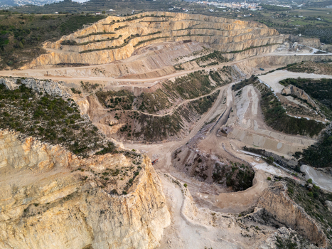 Aerial view of a large open pit stone quarry with terraced rock faces excavated earth and winding access roads in Teulada Valencian Community Spain.