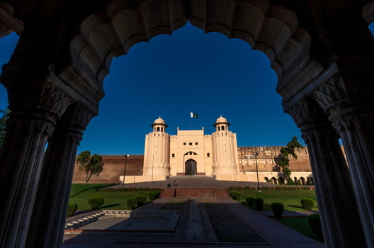 View of Lahore Fort framed by an ornate archway with the historic Alamgiri Gate manicured lawns and a clear blue sky in Lahore Punjab Pakistan.