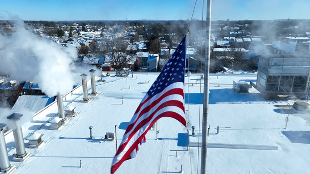 Aerial view of an American flag waving on a snowy rooftop with steam rising from vents above the town of Lancaster Pennsylvania United States.