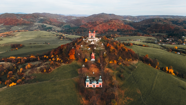 Aerial view of the Kalvaria Banska Stiavnica complex with its red Baroque chapels on a hill surrounded by vibrant autumn foliage and rolling hills in Banska Stiavnica Banskobystricky kraj Slovakia.