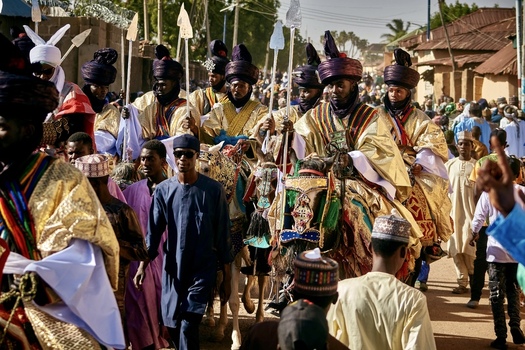 Zaria city Nigeria 21 March 2026 View of a vibrant procession of horsemen in resplendent golden robes and ornate turbans parading through a lively street amidst a cheering crowd. Zaria city Nigeria 21 March 2026 View of a vibrant procession of horsemen in resplendent golden robes and ornate turbans parading through a lively street amidst a cheering crowd.