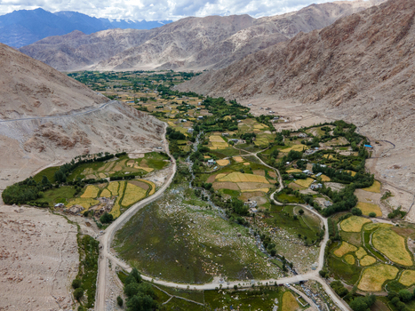 Aerial view of the lush green agricultural fields and a winding river nestled between the rugged arid mountain ranges of the Ladakh valley in Ladakh Division Ladakh India. Aerial view of the lush green agricultural fields and a winding river nestled between the rugged arid mountain ranges of the Ladakh valley in Ladakh Division Ladakh India.