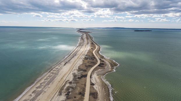 Aerial view of the Powder Point Bridge cutting a graceful line through the shimmering turquoise waters under a sky brushed with wispy clouds Duxbury Massachusetts United States.