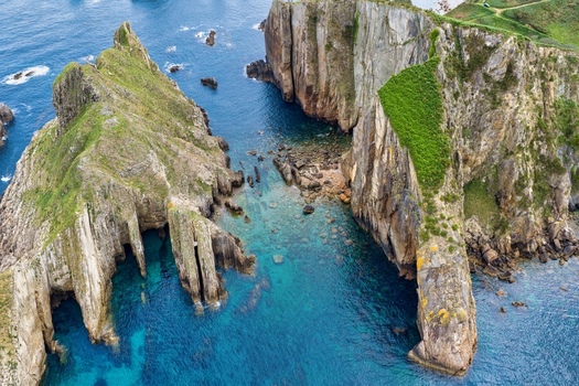 Aerial view of Silence Beach Viewpoint with dramatic jagged cliffs turquoise ocean waters and lush green vegetation on the rocks Cudillero Asturias Spain.