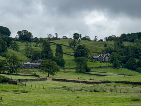 View of rolling green hills and traditional dry stone walls surrounding a stone farmhouse under a cloudy sky in the Yorkshire Dales near Hawes England United Kingdom. View of rolling green hills and traditional dry stone walls surrounding a stone farmhouse under a cloudy sky in the Yorkshire Dales near Hawes England United Kingdom.