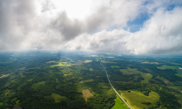Aerial view of a rural landscape with lush green forests agricultural fields and a road stretching into the distance under a cloudy sky in Latvia. Aerial view of a rural landscape with lush green forests agricultural fields and a road stretching into the distance under a cloudy sky in Latvia.