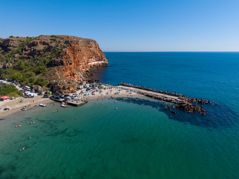 Aerial view of Bolata beach with its distinctive reddish cliffs turquoise bay breakwater and people enjoying the sunny day in Dobrich Province Bulgaria.