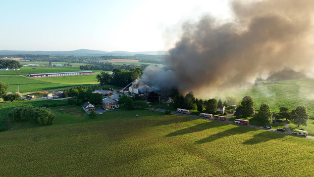 Rapho Township Pennsylvania United States 05 July 2023 Aerial view of a large fire at a rural property with emergency vehicles and thick smoke rising over the fields.