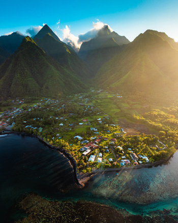 Aerial view of lush volcanic peaks and a coastal village nestled along the turquoise lagoon during golden hour in Moorea Maiao Windward Islands French Polynesia. Aerial view of lush volcanic peaks and a coastal village nestled along the turquoise lagoon during golden hour in Moorea Maiao Windward Islands French Polynesia.