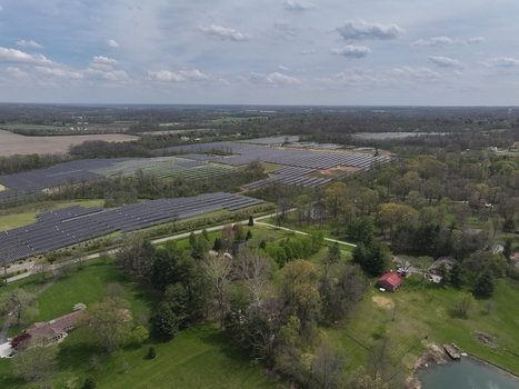 Lebanon United States 12 April 2026 Aerial view of a large solar farm array surrounded by green fields residential houses and dense trees under a cloudy sky.