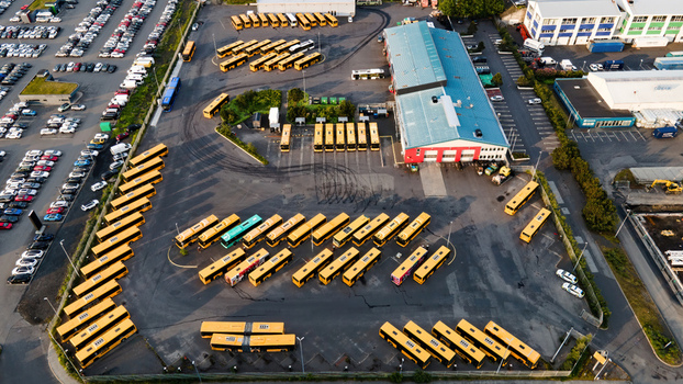 Aerial view of a bus depot with rows of yellow buses maintenance facilities and tire tracks on the asphalt surface in Reykjavik Reykjavikurborg Iceland.