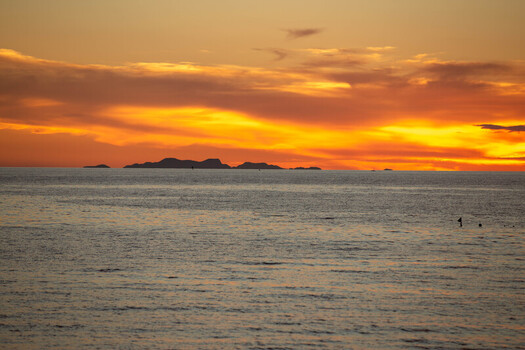 View of the silhouette of Bantayan Island against a vibrant orange and yellow sunset sky over the calm sea in Cebu Central Visayas Philippines. View of the silhouette of Bantayan Island against a vibrant orange and yellow sunset sky over the calm sea in Cebu Central Visayas Philippines.