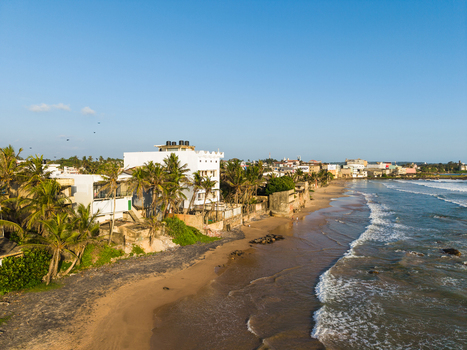 Aerial view of the sandy coastline with white buildings and palm trees along the shore under a clear blue sky in Galle Southern Province Sri Lanka.