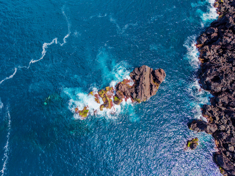 Aerial view of the rugged dark volcanic rocks contrasting with the turquoise sea where frothy white waves crash around the Prainha coastline Pico Azores Portugal. Aerial view of the rugged dark volcanic rocks contrasting with the turquoise sea where frothy white waves crash around the Prainha coastline Pico Azores Portugal.