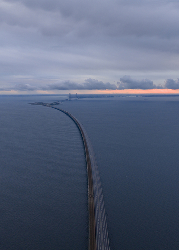 Aerial view of the Great Belt Bridge stretching across the dark blue sea under a dramatic cloudy sky at twilight in Denmark. Aerial view of the Great Belt Bridge stretching across the dark blue sea under a dramatic cloudy sky at twilight in Denmark.