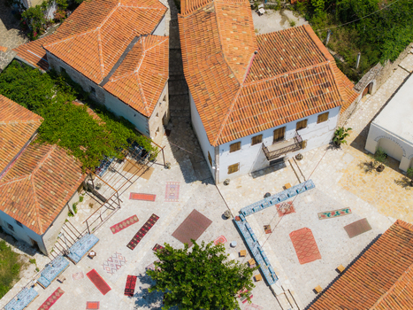 Aerial view of traditional white houses with terracotta roofs and colorful carpets spread across a stone courtyard in Dhermi Vlore County Albania. Aerial view of traditional white houses with terracotta roofs and colorful carpets spread across a stone courtyard in Dhermi Vlore County Albania.
