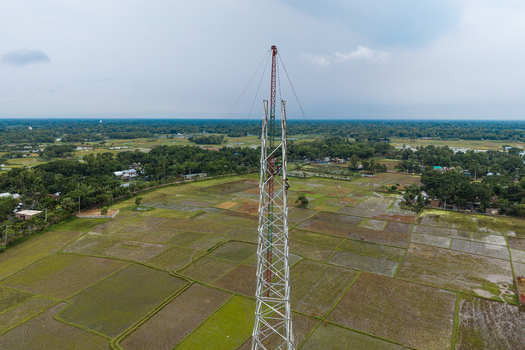 Trishal Upazila Bangladesh 13 May 2026 Aerial view of a tall telecommunications tower under construction with workers on the structure surrounded by green agricultural fields. Trishal Upazila Bangladesh 13 May 2026 Aerial view of a tall telecommunications tower under construction with workers on the structure surrounded by green agricultural fields.