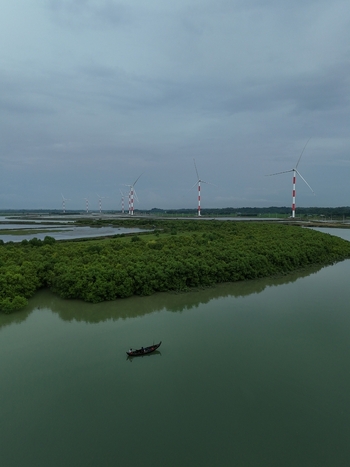 Aerial view of Khurushkul wind power plant with turbines standing along lush green mangroves and a small boat floating on calm water in Cox s Bazar Chittagong Division Bangladesh. Aerial view of Khurushkul wind power plant with turbines standing along lush green mangroves and a small boat floating on calm water in Cox s Bazar Chittagong Division Bangladesh.