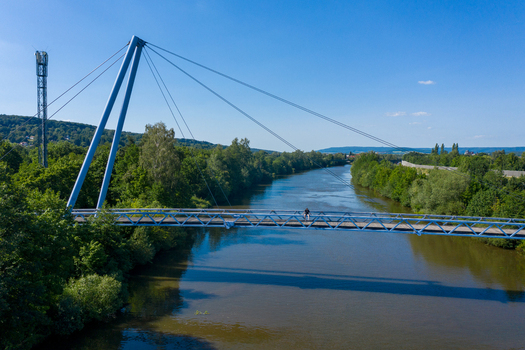 Aerial view of the Sportinsel Forchheim bridge over the Regnitz river with a person sitting on the railing surrounded by dense green trees Forchheim Bayern Germany.