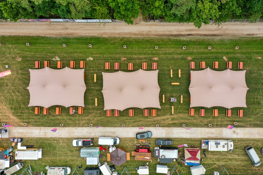 Herzogenaurach Germany 25 July 2025 Aerial view of the Open Beatz Festival featuring large white canopies and wooden picnic tables arranged on a green field next to a forest. Herzogenaurach Germany 25 July 2025 Aerial view of the Open Beatz Festival featuring large white canopies and wooden picnic tables arranged on a green field next to a forest.