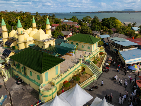 Aerial view of Sultan Riau Grand Mosque with its yellow walls and green domes overlooking the sea in Tanjung Pinang Kota Riau Islands Indonesia. Aerial view of Sultan Riau Grand Mosque with its yellow walls and green domes overlooking the sea in Tanjung Pinang Kota Riau Islands Indonesia.