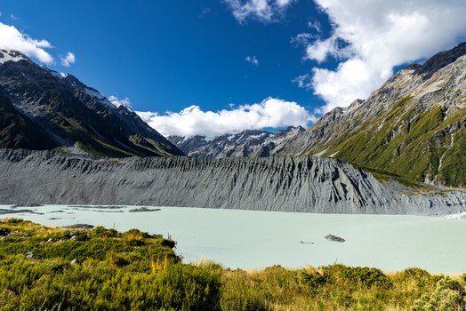 View of a glacial landscape with rugged mountains and a milky turquoise lake under a vibrant blue sky with scattered clouds Mount Cook Canterbury Region New Zealand. View of a glacial landscape with rugged mountains and a milky turquoise lake under a vibrant blue sky with scattered clouds Mount Cook Canterbury Region New Zealand.