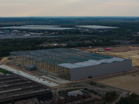Aerial view of a large industrial construction site featuring a steel frame structure and expansive warehouse development in the United Kingdom. Aerial view of a large industrial construction site featuring a steel frame structure and expansive warehouse development in the United Kingdom.