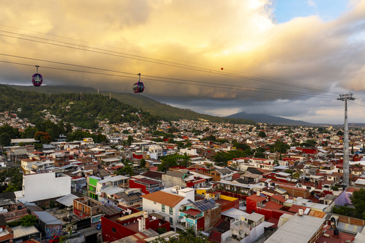 Aerial view of the Teleferico cable car system gliding over dense urban rooftops at sunset with mountains in the background in Uruapan Michoacan Mexico.