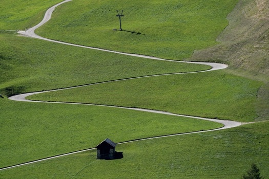 View of the winding serpentine road of the Sankt Gotthard Pass crossing lush green alpine meadows with a small wooden hut Airolo Ticino Switzerland.