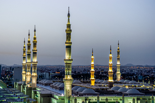 View of Al Masjid e Nabawi with its illuminated minarets at dusk overlooking the city of Madinah Al Madinah Province Saudi Arabia.