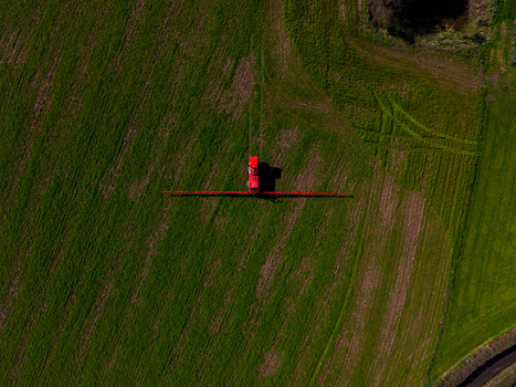 Aerial view of a red tractor spraying a green field at Gnosall Heath Gnosall England United Kingdom. Aerial view of a red tractor spraying a green field at Gnosall Heath Gnosall England United Kingdom.