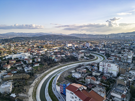 Aerial view of the Gjanica River winding through the urban landscape of Fier featuring residential buildings rooftops and distant mountains in Fier Fier County Albania.