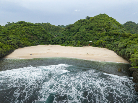 Aerial view of Sedahan Beach with foamy waves meeting golden sand and lush green hills Gunungkidul Regency Special Region of Yogyakarta Indonesia. Aerial view of Sedahan Beach with foamy waves meeting golden sand and lush green hills Gunungkidul Regency Special Region of Yogyakarta Indonesia.