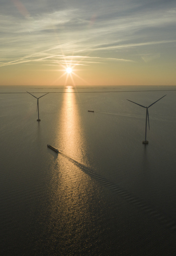 Aerial view of offshore wind turbines and a cargo ship sailing on the calm sea during a golden sunset Netherlands. Aerial view of offshore wind turbines and a cargo ship sailing on the calm sea during a golden sunset Netherlands.