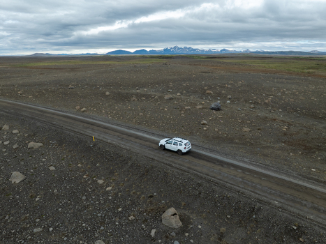 Aerial view of a white SUV driving on a gravel road through the rugged volcanic landscape of Kerlingarfjoll with distant mountains under a cloudy sky in Hrunamannahreppur Iceland. Aerial view of a white SUV driving on a gravel road through the rugged volcanic landscape of Kerlingarfjoll with distant mountains under a cloudy sky in Hrunamannahreppur Iceland.