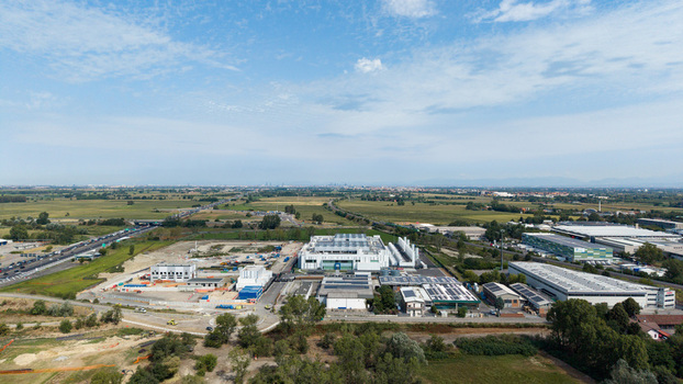 Aerial view of a modern data center campus with industrial buildings solar panels and surrounding green fields near a highway in Melegnano Lombardy Italy.
