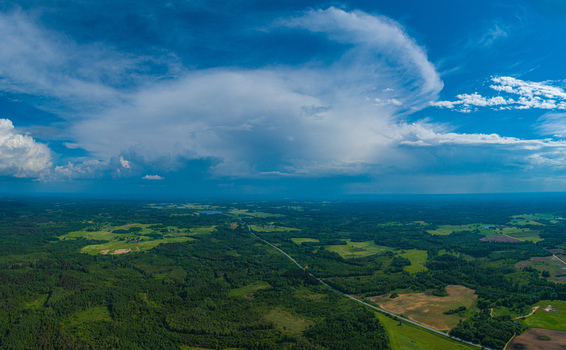 Aerial view of a rural landscape with lush green forests agricultural fields and a road stretching into the distance under a dramatic cloud formation in Latvia. Aerial view of a rural landscape with lush green forests agricultural fields and a road stretching into the distance under a dramatic cloud formation in Latvia.