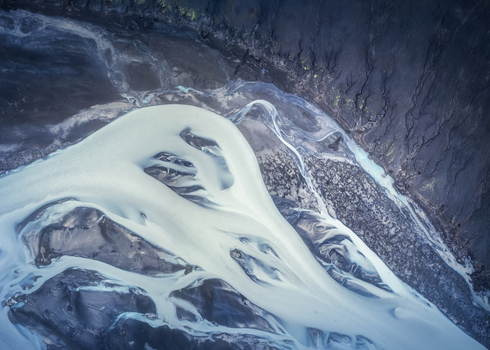 Aerial view of the braided glacial river in Fjallabak Nature Reserve with milky blue water flowing through dark volcanic terrain in Rangarthing ytra Iceland.