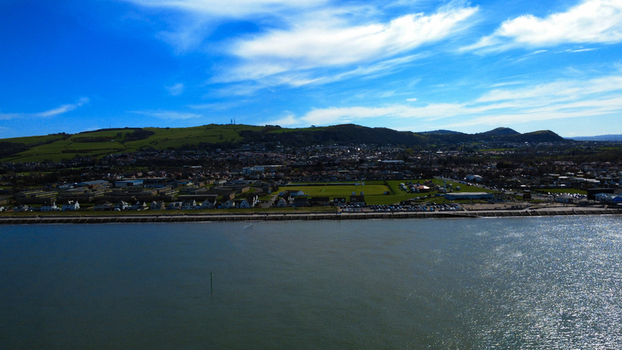 Aerial view of the coastline meeting the town below the lush green hills under a bright blue sky Prestatyn Wales United Kingdom. Aerial view of the coastline meeting the town below the lush green hills under a bright blue sky Prestatyn Wales United Kingdom.