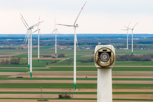 Aerial view of wind turbines standing in agricultural fields with a close up of a nacelle in the foreground under a cloudy sky in Debsk Masovian Voivodeship Poland.