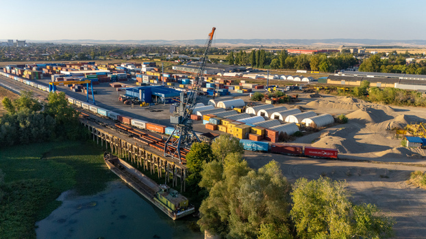Sremska Mitrovica Serbia 16 September 2026 Aerial view of the industrial port with shipping containers a large crane freight trains and a barge moored on the riverbank. Sremska Mitrovica Serbia 16 September 2026 Aerial view of the industrial port with shipping containers a large crane freight trains and a barge moored on the riverbank.
