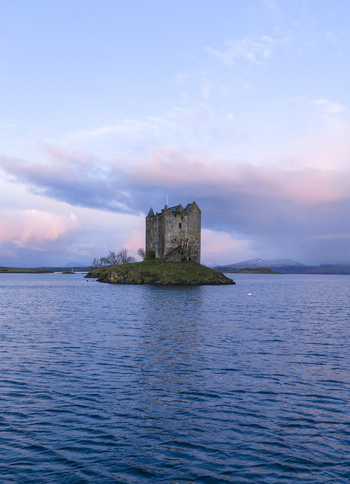 Aerial view of Castle Stalker on a small island surrounded by calm blue water under a soft sunset sky Appin Scotland United Kingdom. Aerial view of Castle Stalker on a small island surrounded by calm blue water under a soft sunset sky Appin Scotland United Kingdom.