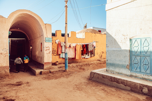 View of a traditional Nubian village street with children walking through an arched entrance and laundry hanging on a yellow wall in Aswan Aswan Governorate Egypt. View of a traditional Nubian village street with children walking through an arched entrance and laundry hanging on a yellow wall in Aswan Aswan Governorate Egypt.