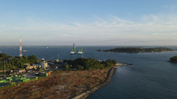 Aerial view of the port of Sorong with large cranes shipping containers and coastal vegetation along the sea in Sorong Southwest Papua Indonesia. Aerial view of the port of Sorong with large cranes shipping containers and coastal vegetation along the sea in Sorong Southwest Papua Indonesia.