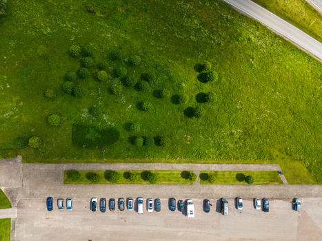 Aerial view of a parking lot with various cars parked in rows next to a green field with scattered trees and a road in Kaunas Kaunas County Lithuania.