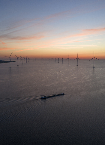 Aerial view of the IJsselmeer offshore wind farm with turbines standing in calm water under a sunset sky and a barge passing by Netherlands.