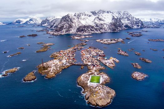 Aerial view of the iconic football pitch in the fishing village of Henningsvaer surrounded by the sea and snow capped mountains in the Lofoten archipelago in Nordland Norway.