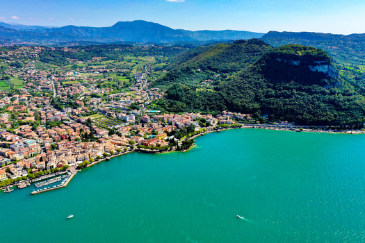 Aerial view of Lake Garda with the coastal town buildings lush green hills and turquoise water under a clear blue sky in Italy. Aerial view of Lake Garda with the coastal town buildings lush green hills and turquoise water under a clear blue sky in Italy.