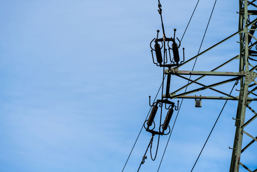 View of a high voltage electricity pylon with insulators and power lines set against a clear blue sky in Poland.